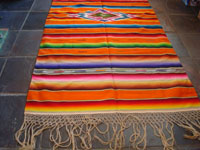 Mexican vintage textiles, and Mexican vintage Saltillo sarapes and huipiles, a beautiful Saltillo sarape (serape) with a lovely orange background and a stunning center medallion of silk and wool, c. 1930's.  Closeup photo of one edge of the Saltillo serape showing the fringe.