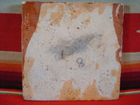 Mexican vintage pottery and folk art, a tile with terra cotta background and a scene of a Mexican campesino carrying large jarros or jugs, Tlaquepaque, c. 1940's. Photo of the back side of the tile.