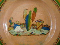 Mexican vintage pottery and ceramics, a lovely terra-cota plate from Tlaquepaque, Jalisco, c. 1940. The peach-colored background glazing is beautiful. The scene on the plate is exceptional; it features a snoozing campesino in a wonderful rural setting. Closeup of the central design, showing the snoozing campesino amidst rocks and plants.