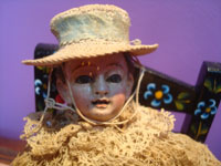 Mexican vintage devotional art, a small statue of the Santo Nino de Atocha, with its hat and original clothes, and seated on a colorful wooden Mexican chair, Mexico, 19th century.  Closeup photo of the santo's face.